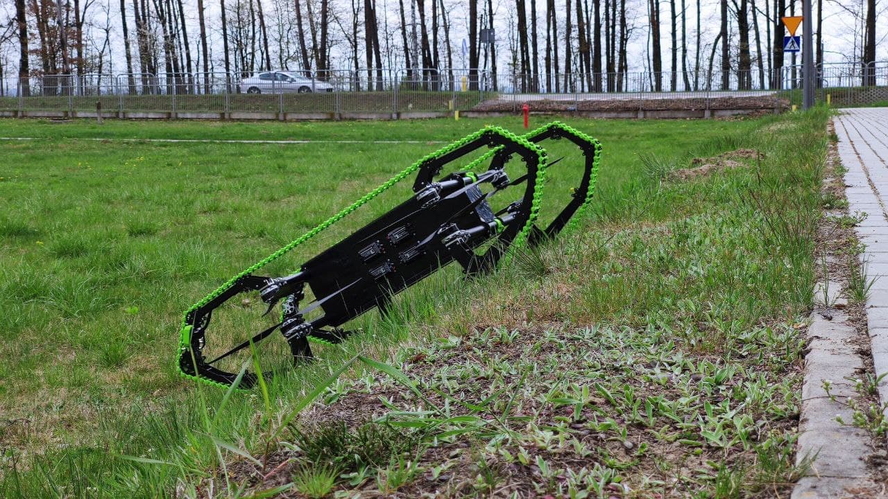 HUUVER hybrid drone at rest on terrain, tracked drive units and VTOL rotor arms visible.